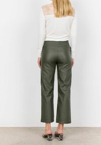 Zielone spodnie z szerokimi nogawkami z ekologicznej skóry, gładka tekstura, fason z wysokim stanem, połączone z białą bluzką z długim rękawem z koronkowym tylnym panelem.