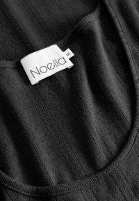 Čierny tielko s ryhovanou textúrou, má okrúhly výstrih a etiketu s nápisom "Noella" a veľkosť „S“ na bielej prešitej nášivke.