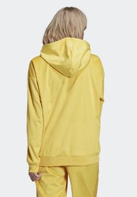 Gul velourhoodie med stor huva, ribbad textur och lös passform. Baksidan har en enkel design utan detaljer.