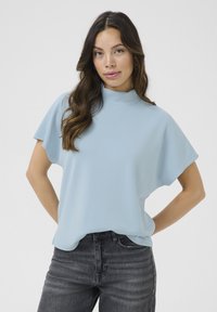 Light blue short-sleeve top with a high neckline, smooth texture, and relaxed fit. Paired with dark gray jeans featuring subtle fading.