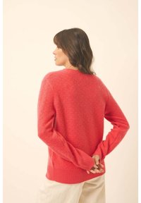 Helles Korallenpullover mit strukturiertem Strick, geripptem Saum und Bündchen sowie einer lässigen Passform. Rückwärts getragen, zeigt das detaillierte Rückendesign.