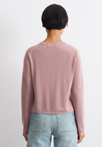 Pull-over rose à manches longues en matière tricotée douce, avec un col rond et des poignets élastiques. Conçu avec une coupe courte.