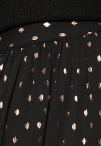 Svart tyg med en strukturerad stickad topp, som har en plisserad kjol prydd med metalliska bronsprickar i olika storlekar.