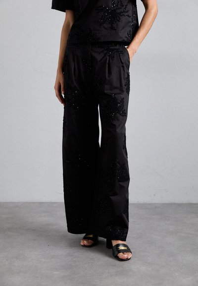 Pantalons noirs à coupe large, avec des motifs floraux en perles complexes. Tissu lisse et texturé avec une jambe large et des poches latérales.