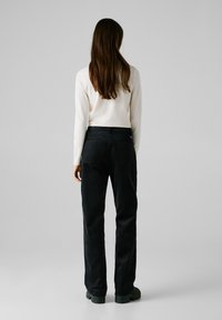 Schwarze Cord-Hose mit geradem Bein, ausgestattet mit zwei Gesäßtaschen und einer strukturierten Oberfläche, kombiniert mit einem weißen Langarmoberteil.