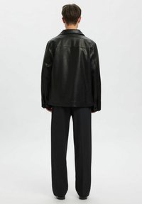 Mustast nahast jakk, millel on sile pind ja liialdatud suurus, millel on sälguline krae ja nööbitud varrukad, kantud lahtiste tumedate pükste kohal.