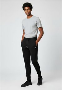 Camiseta gris de manga corta combinada con joggers negros de corte ajustado que tienen bolsillos laterales y cinturilla elástica, usados con zapatillas negras.