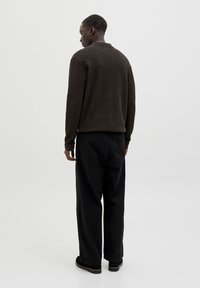 Brauner Strickpullover mit geripptem Ausschnitt, kombiniert mit lockeren schwarzen Hosen. Der Stoff erscheint strukturiert und die Silhouette ist lässig.