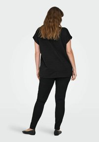 Svart oversized t-shirt med korta ärmar, tillverkad av ett mjukt tyg. Kombinerat med svarta skinny jeans och platta skor, sedd bakifrån.