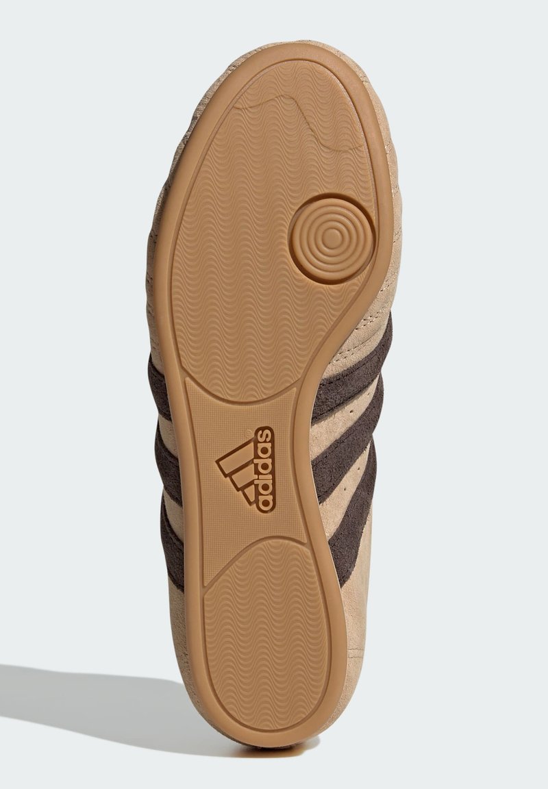 Suela de zapatilla en tonos marrones y beige con goma texturizada, que presenta rayas alternas y un logo embossado en un patrón circular.