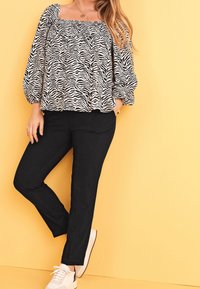 Sort-hvid zebraprint bluse med puffærmer, parret med sorte bukser og hvide sneakers. Baggrunden er en ensfarvet gul farve.