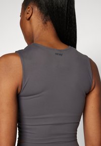 Szürke sportos crop top, testhezálló fazonnal, kerek nyakkivágással és ujjatlan kivitelben. Hátsó részén diszkrét márkázás található, sima tapintású anyagból készült.