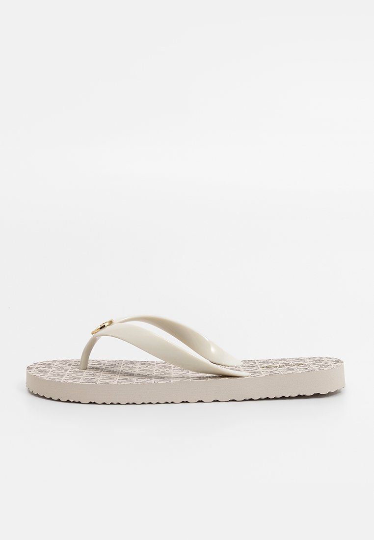 Sandale en toile de couleur beige avec une semelle texturée, des brides lisses et un petit accent doré sur l'une des brides. Design plat, léger et style décontracté.