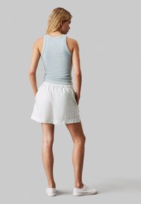 Top de tirantes de color azul claro con costuras acanaladas, combinado con pantalones cortos blancos que presentan un sutil patrón de rayas, cinturilla elástica y bolsillos laterales.