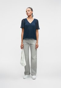 Μπλε πουκάμισο με διαφανή κοντά μανίκια, συνδυασμένο με ανοιχτού γκρι παντελόνι φάρδους. Τα αξεσουάρ περιλαμβάνουν μια λευκή τσάντα χεριού και λευκά αθλητικά παπούτσια.