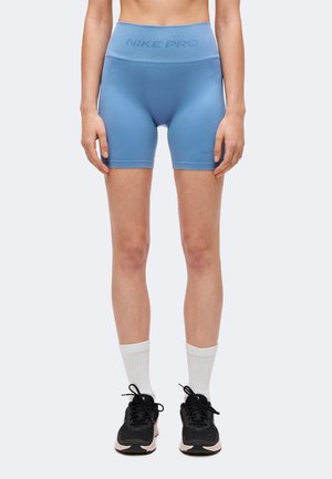 Person iført lyseblå Nike Pro kompressionsshorts, hvide crew-sokker og sorte løbesko, stående foran en ensfarvet baggrund.