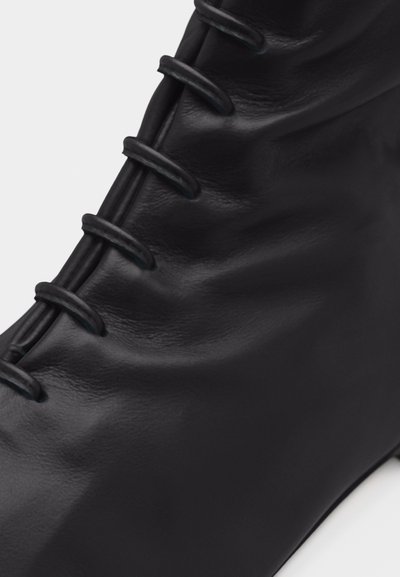 Κοντινό πλάνο μαύρης δερμάτινης μπότας με ορατούς βρόχους κορδονιών και λείωσε, ελαφρώς υφασμένο επιφάνεια.