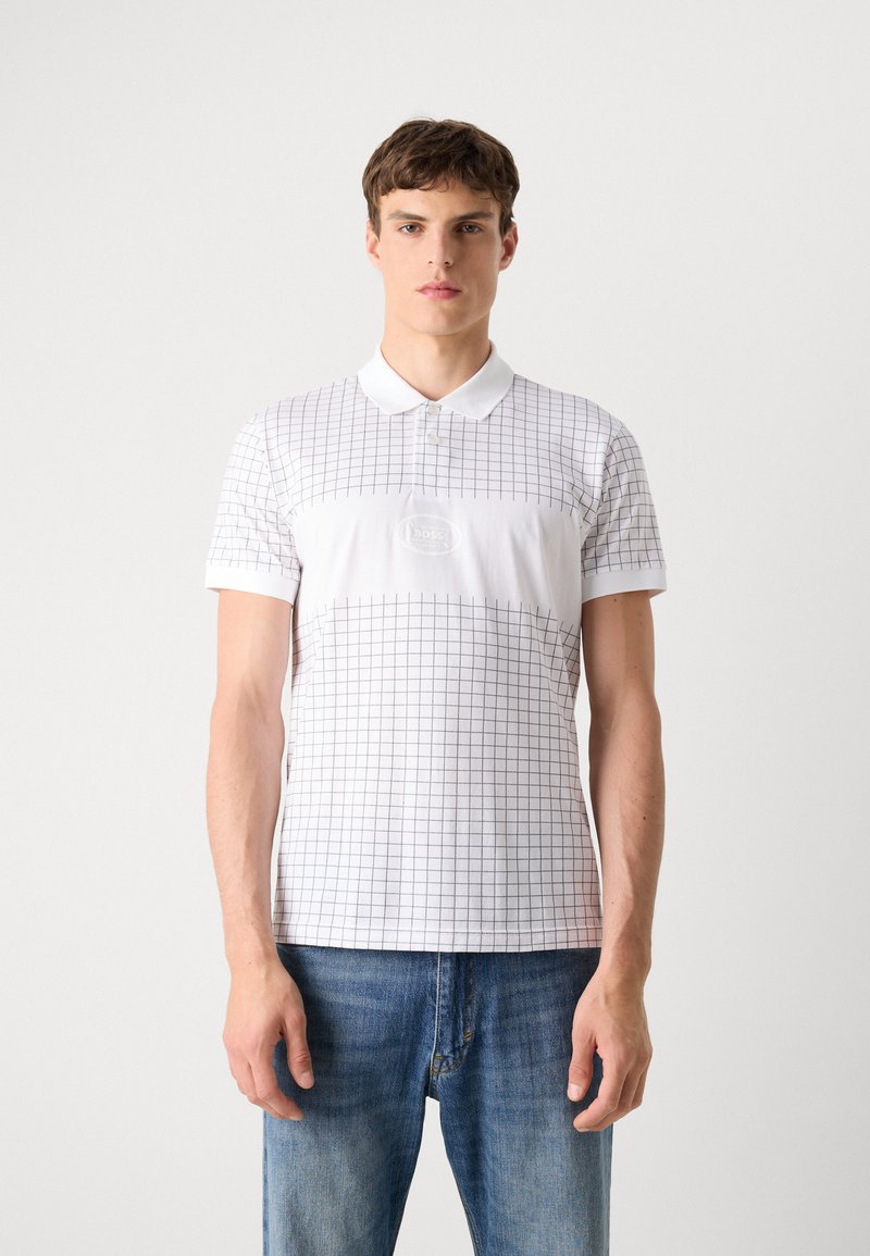 Camisa polo blanca con un patrón de cuadrícula, mangas cortas y un cuello clásico. Presenta un parche con el logo central y está hecha de un suave material de algodón.