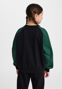 Svart sweatshirt med gröna raglanärmar, strukturerad tyg och rund halsringning. Har en avslappnad passform och ribbade muddar och nederkant.