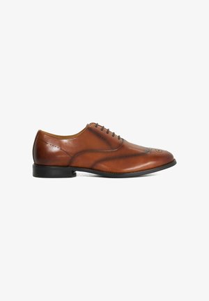 Chaussure habillée Oxford pour homme en cuir marron avec détails brogue et semelle noire, vue de profil sur fond blanc.
