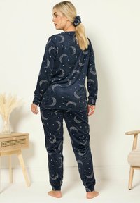 Set di pigiama navy con maniche lunghe e pantaloni decorati con motivi a luna crescente e stelle, realizzato in tessuto morbido con polsini elasticizzati.