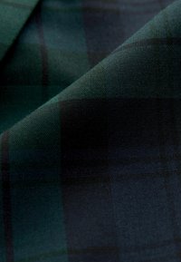 Tartanová látka v tmavě zelené a černé barvě, s kostkovaným vzorem a hladkým, texturovaným povrchem. Měkký materiál s volně splývavými vrstvami.