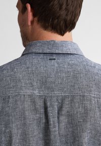 Camicia da uomo con un motivo a righe grigie e bianche, colletto, dettagli di cucitura sottili e un'etichetta situata vicino al colletto.