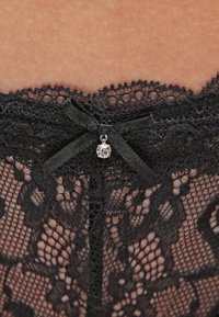 Schwarze Spitzenunterwäsche mit floralen Mustern, einem gewellten Rand und einem Satinbandakzent mit einem kleinen Edelsteindetail in der Mitte.