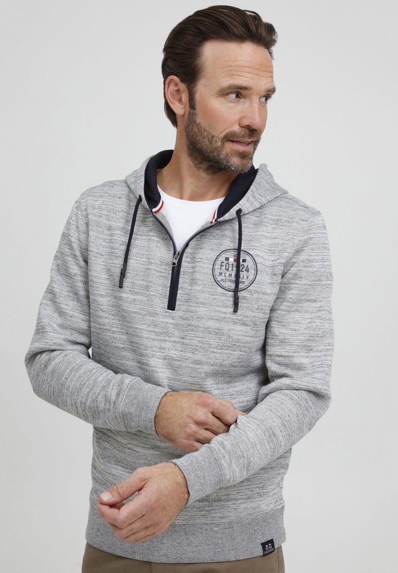 Gray heathered hoodie with a zip neck, navy accents, and a circular logo patch. Features long sleeves and ribbed cuffs. Textured fabric.