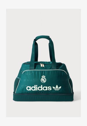 Τουρκουάζ αθλητική τσάντα Adidas με λευκό λογότυπο, έμβλημα της Ρεάλ Μαδρίτης, διπλές χειρολαβές στην κορυφή, θήκες με φερμουάρ και δίχτυα στις πλαϊνές τσέπες.