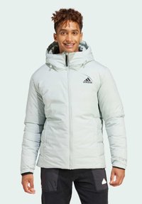 Lichtblauwe pufferjack met een capuchon, voorzien van een zwart Adidas-logo op de borst en elastische manchetten voor een goede pasvorm.