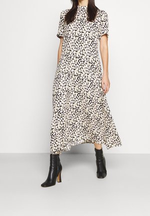 Donna che indossa un vestito midi bianco e nero a pois con maniche corte e stivaletti neri con tacco, in piedi contro uno sfondo bianco uniforme.