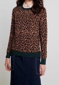 Pull en imprimé léopard dans des tons de marron et noir, avec un col et des poignets côtelés verts. Texture douce, coupe décontractée.