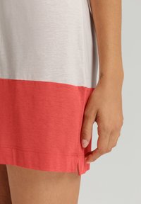Abito color block grigio e corallo con una texture morbida; presenta uno spacco laterale e una vestibilità comoda, mettendo in mostra parte di una mano sull'orlo.