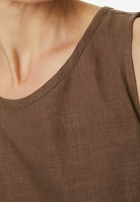 Top sin mangas de lino marrón con un escote amplio y tejido texturizado, centrado en la simplicidad y la comodidad en el diseño.