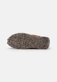 Semelle de chaussure avec une texture tachetée multicolore en caoutchouc recyclé vue du dessous sur un fond blanc uni.
