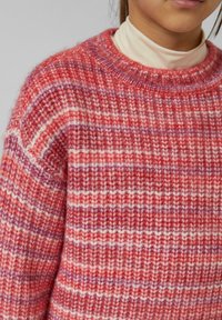 Czerwono-różowy sweter w paski o okrągłym dekolcie, wykonany z teksturowanej mieszanki wełny, o luźnym kroju. Zauważalne miękkie szczegóły z przędzy.