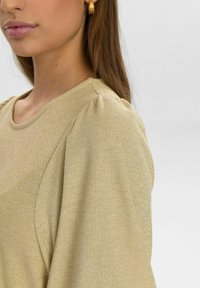 Guld ribbad topp med rund halsringning och puffade korta ärmar, med en subtil lyster och mjuk textur. Accenterad av en slät finish.
