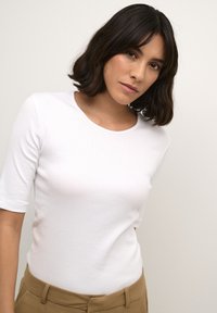 White ribbed short-sleeve top with a round neckline, paired with tan high-waisted pants. Smooth texture; minimal design.