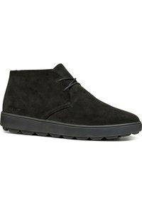 Botas chukka de ante negro con punta redondeada, cordones mínimos y suela de goma texturizada con patrones de tracción ovalados.