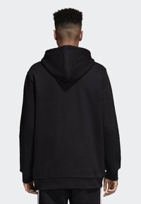 Sudadera negra hecha de tejido suave, con una capucha espaciosa y mangas largas. El diseño es simple, con un corte relajado y sin logotipos visibles.