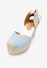 Cuña de espadrille azul claro con suela de yute trenzado, punta redondeada y tira de tela en el tobillo con un acento anudado.