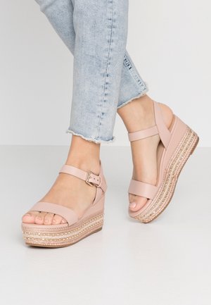 Lyserøde kilehælssandaler med to remme, spænde og en tekstureret flettet platform med gulddetaljer.