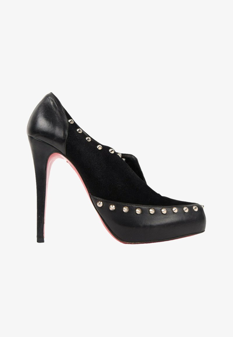 Chaussure à talon haut noire avec garniture cloutée, dessus en daim, talon et bout en cuir, et semelle rouge, vue de profil sur fond blanc.