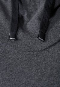Felpa grigia con cappuccio caratterizzata da un tessuto morbido, cordini neri e un piccolo tag con il logo Bench vicino al collo.