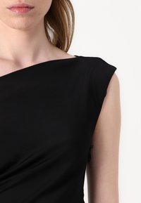 Czarna sukienka bez rękawów z drapowaną konstrukcją. Gładki, miękki materiał o lekkim połysku. Asymetryczny dekolt i elegancki fason.