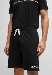 Shorts neri realizzati in morbido tessuto, con vita regolabile tramite cordino, tasche laterali e logo "BOSS" in bianco sulla gamba sinistra.