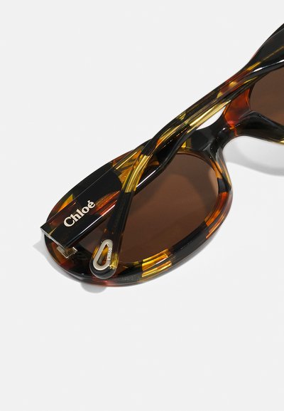 Złożone okulary przeciwsłoneczne w wzór wężowej skorupy z ciemnymi soczewkami i srebrnym metalowym detalem na zauszniku z logo Chloé.