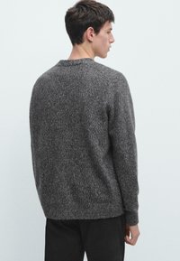 Grå texturerad tröja med rund halsringning, sänkta axlar och långa ärmar; bakifrån visad mot en ljus bakgrund.