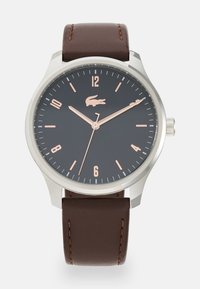 Montre ronde avec un cadran texturé noir, un boîtier en argent et des index heures en or rose. Bracelet en cuir marron avec des coutures contrastées.